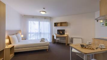 A hotel room with a bed, desk, chair, and a small table with a chessboard.