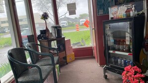 A small cafe with a coffee machine, a refrigerator stocked with beverages, and a few chairs. - Motel Jann (Québec City)