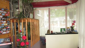 A reception area with a wooden desk, a red carpet, and a window with sheer curtains. - Motel Jann (Québec City)