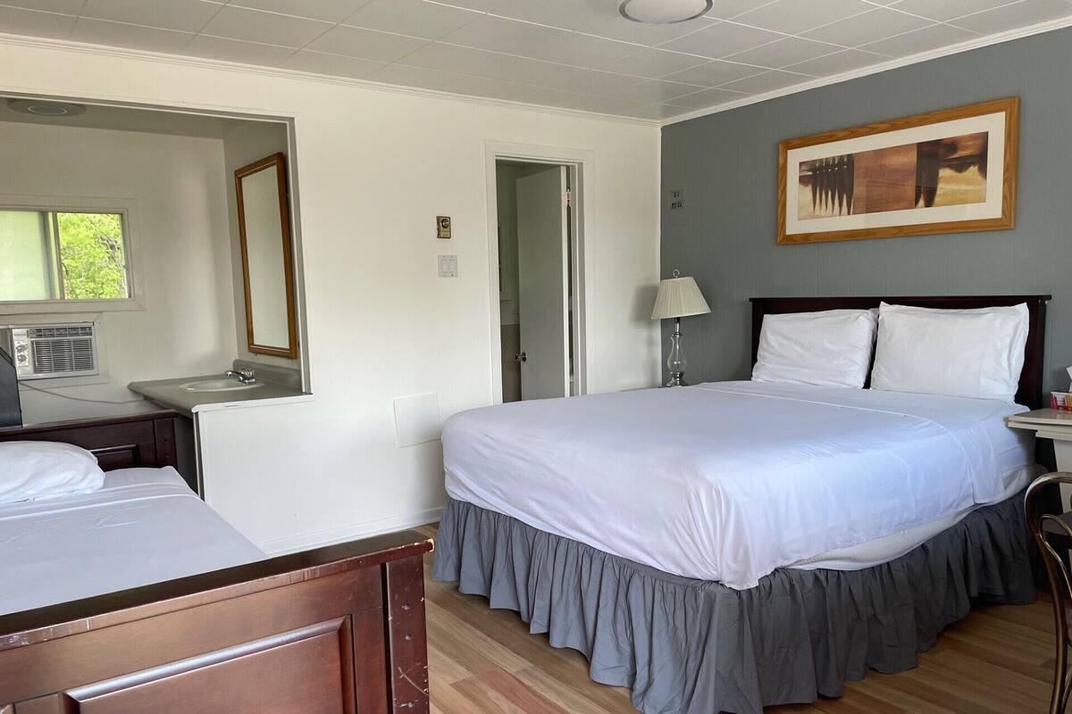 A hotel room with a large bed, a bedside table, a mirror, a window, and a painting on the wall.