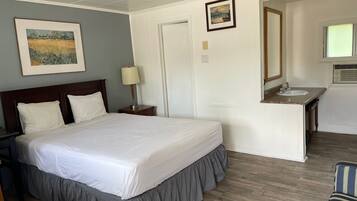 Habitación de hotel con una cama grande, una mesita de noche con lámpara, un baño con lavamanos y espejo, y un cuadro en la pared.
