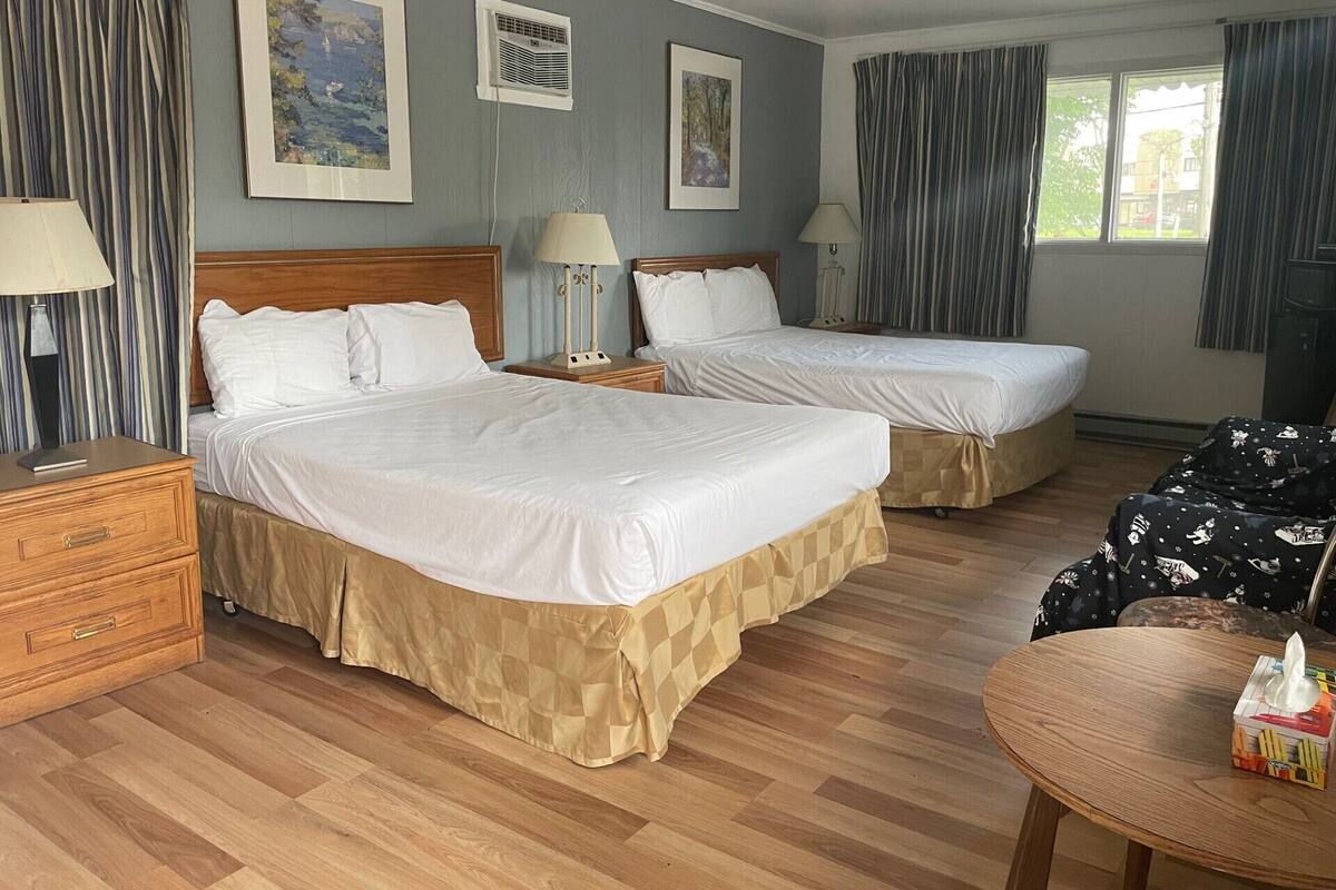 A hotel room with two beds, a wooden dresser, a table with a tissue box, and curtains.