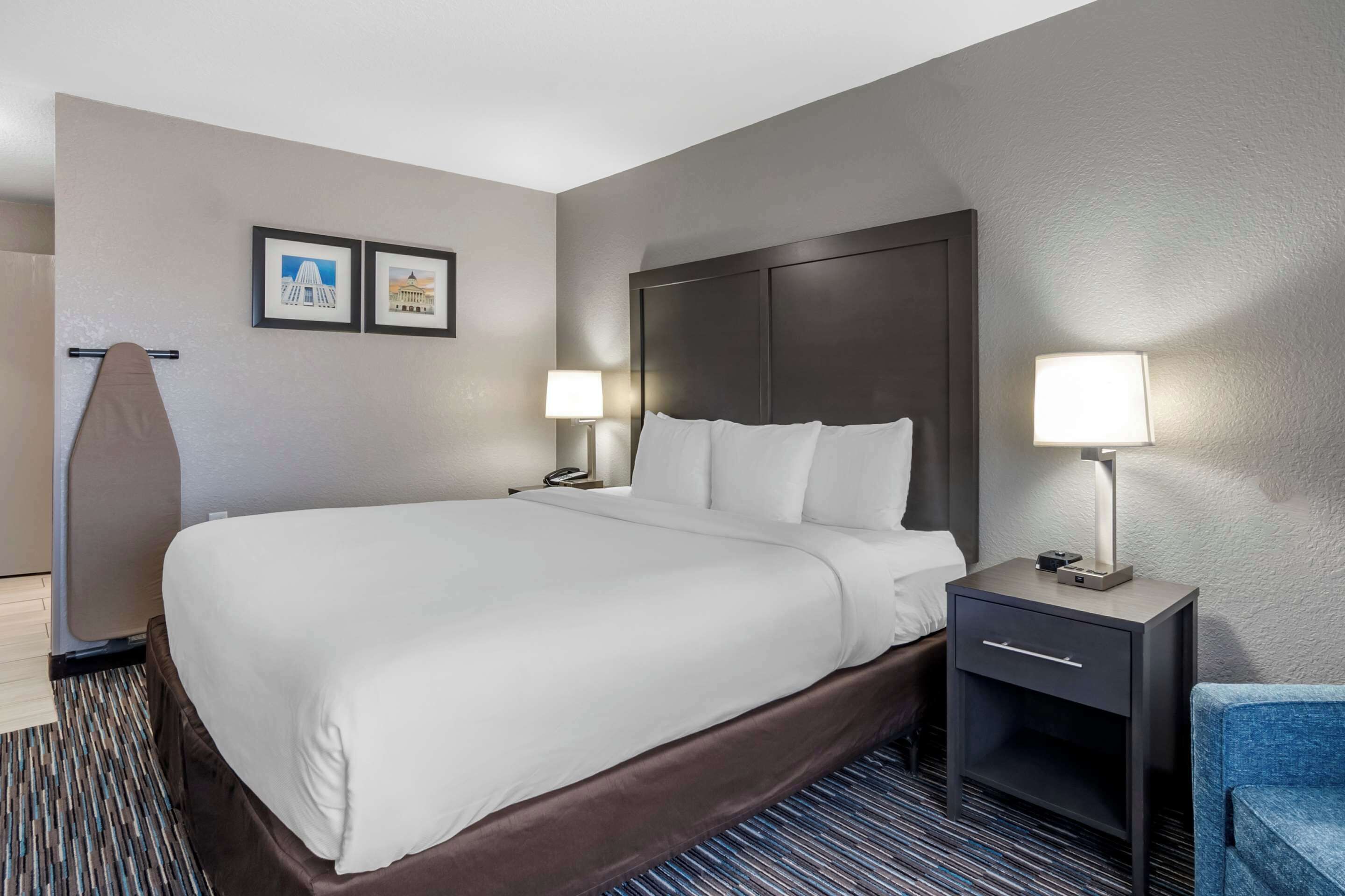 A hotel room with a large bed, two bedside tables with lamps, a chair, and two framed pictures on the wall.