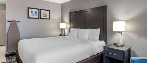 A hotel room with a large bed, two bedside tables with lamps, a chair, and two framed pictures on the wall.