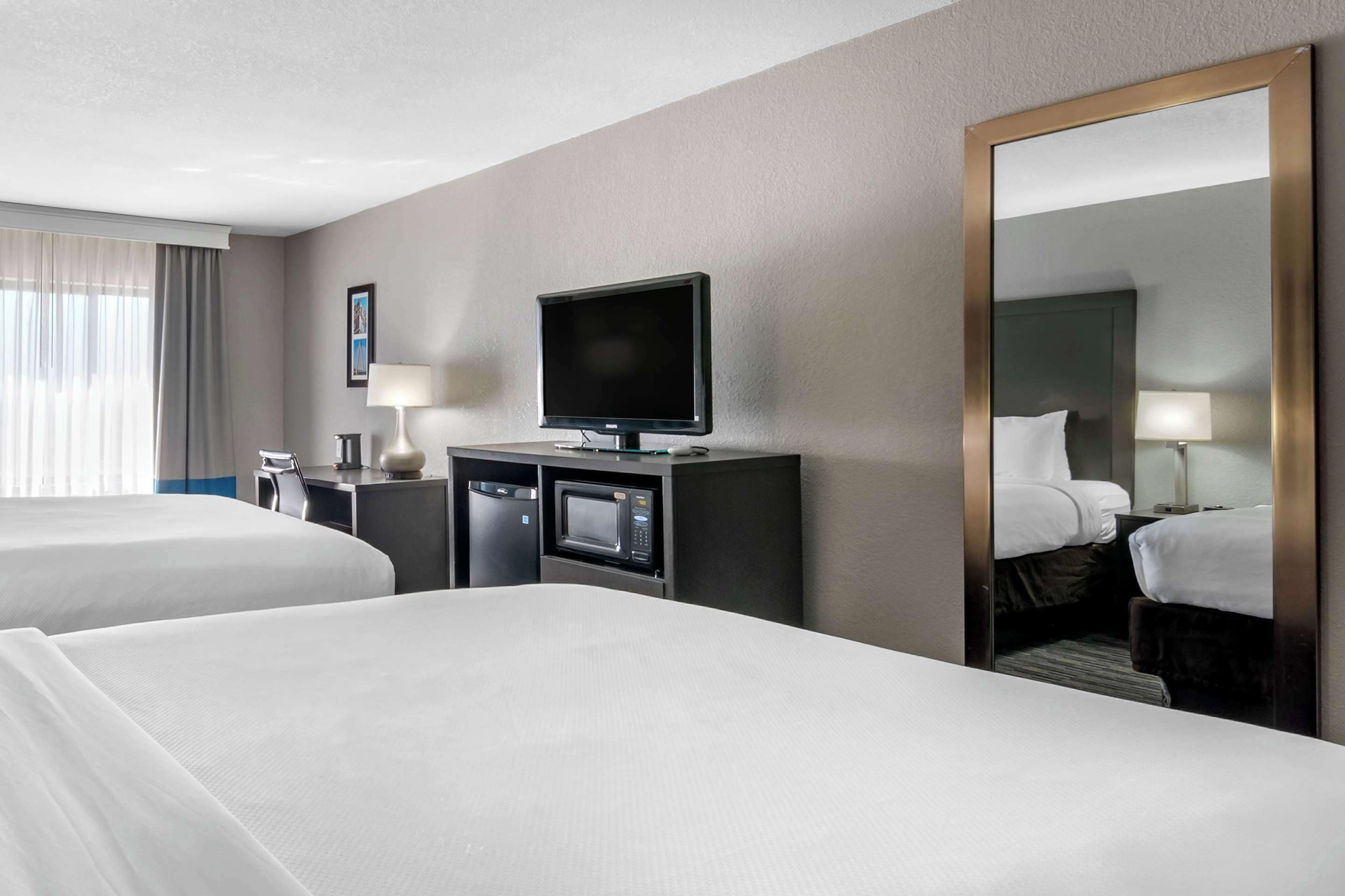 Una habitación de hotel con dos camas, un televisor, un escritorio con un microondas y un espejo grande.