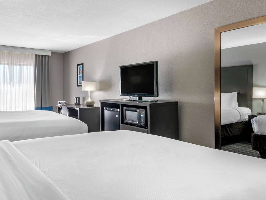 Una habitación de hotel con dos camas, un televisor, un escritorio con un microondas y un espejo grande.