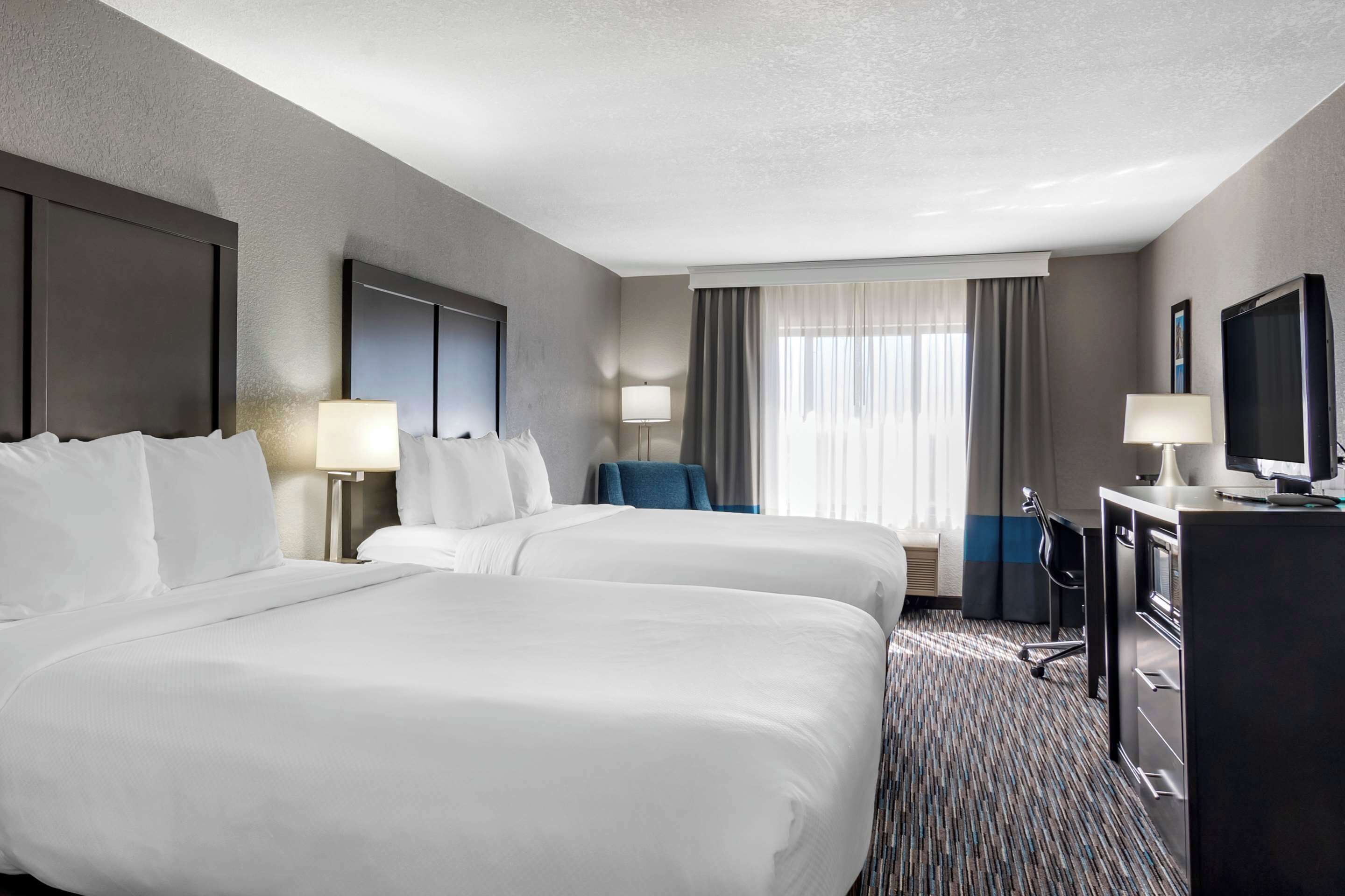 Une chambre d’hôtel avec deux lits, un bureau avec un ordinateur, une télévision et une chaise.