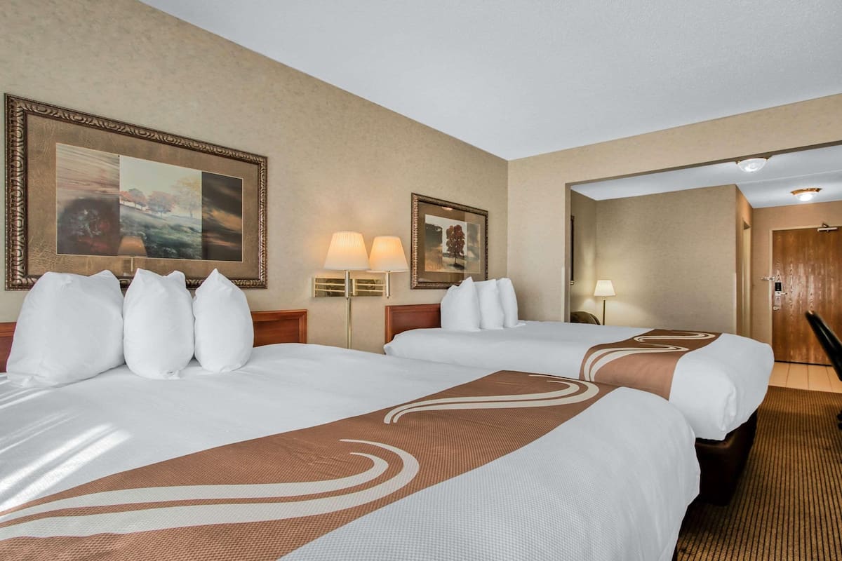A hotel room with two beds, a large framed picture on the wall, a lamp, and a mirror.