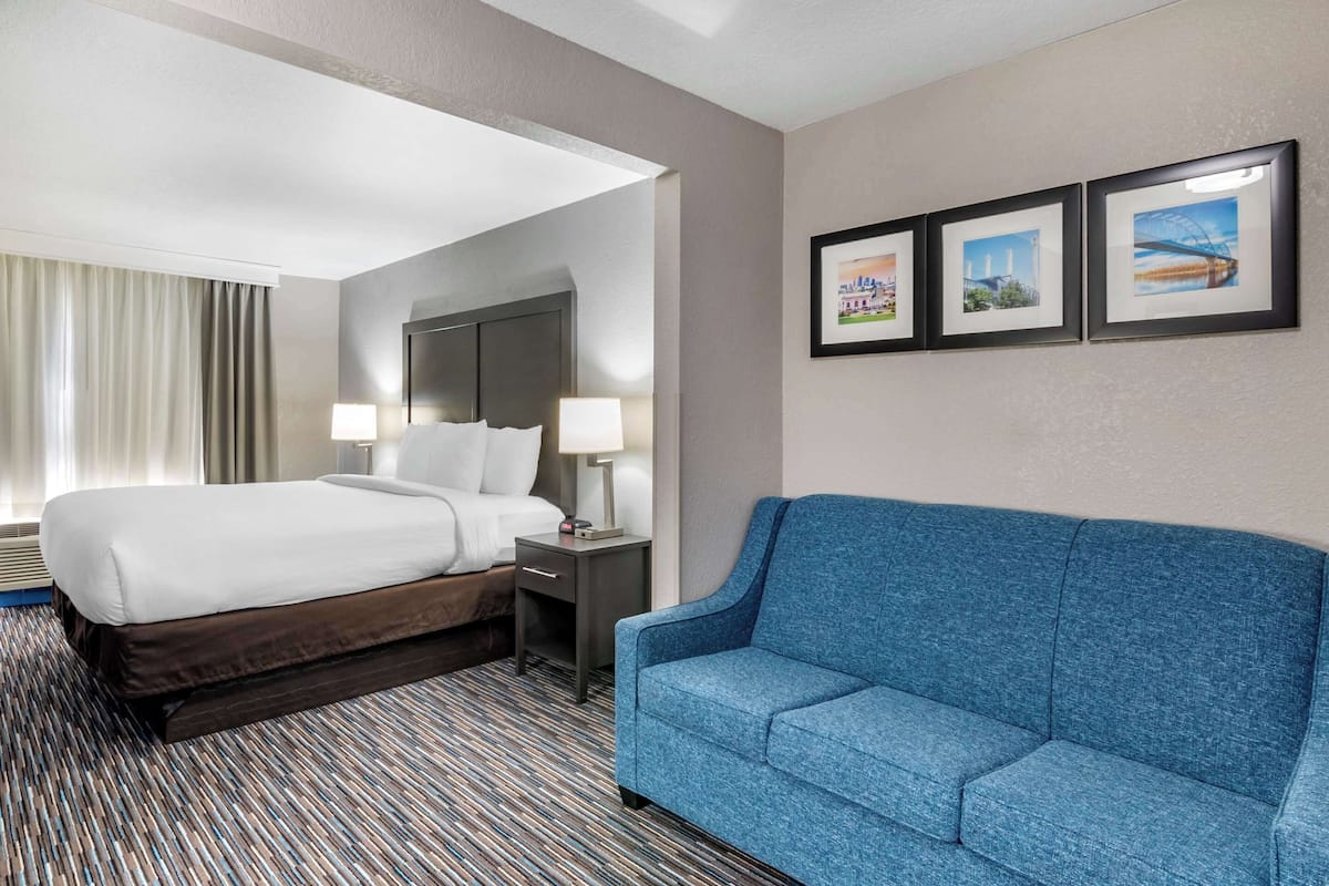 A hotel room with a large bed, a blue sofa, and three framed pictures on the wall.