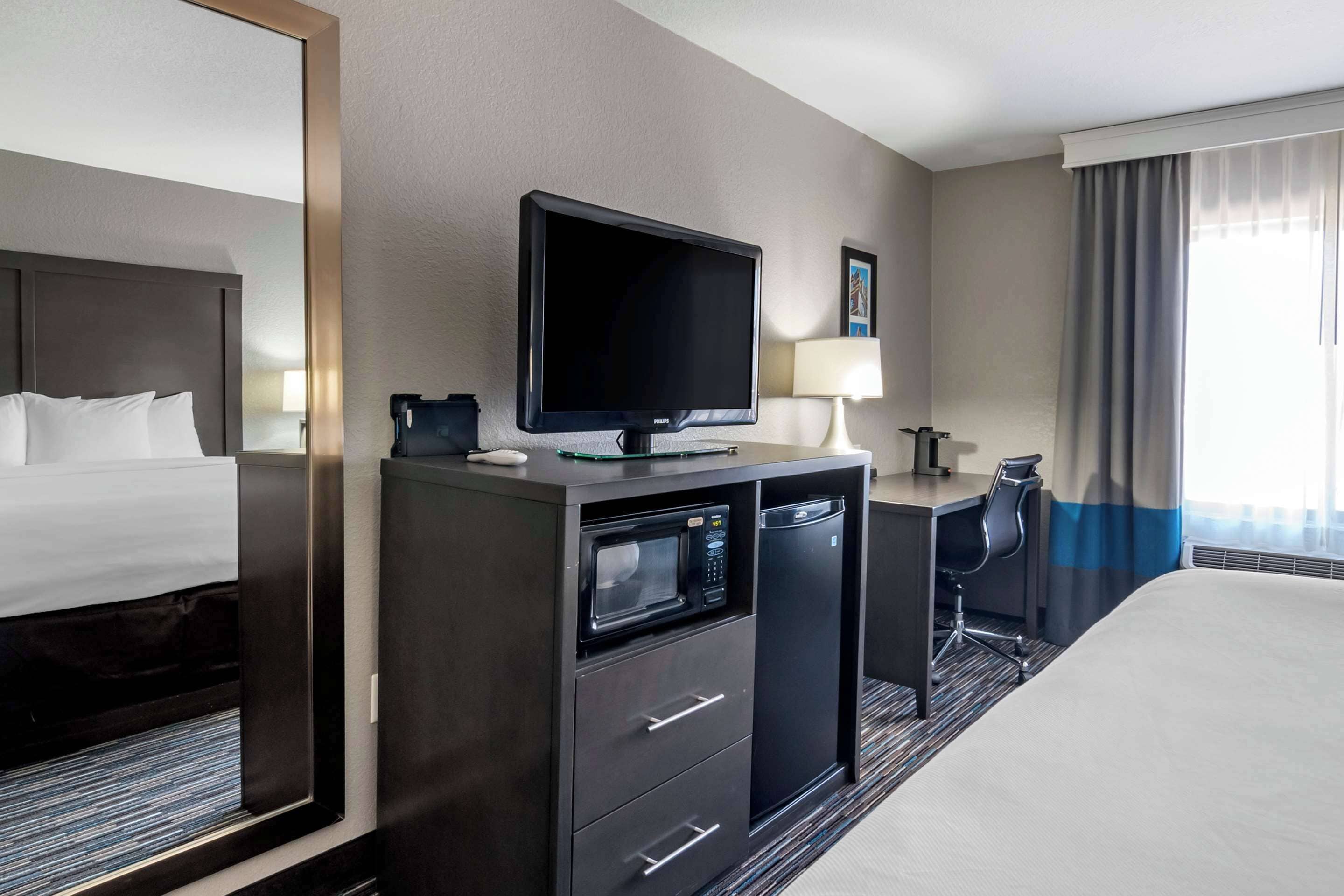 Een hotelkamer met een bed, een bureau met een computer, een magnetron en een televisie.
