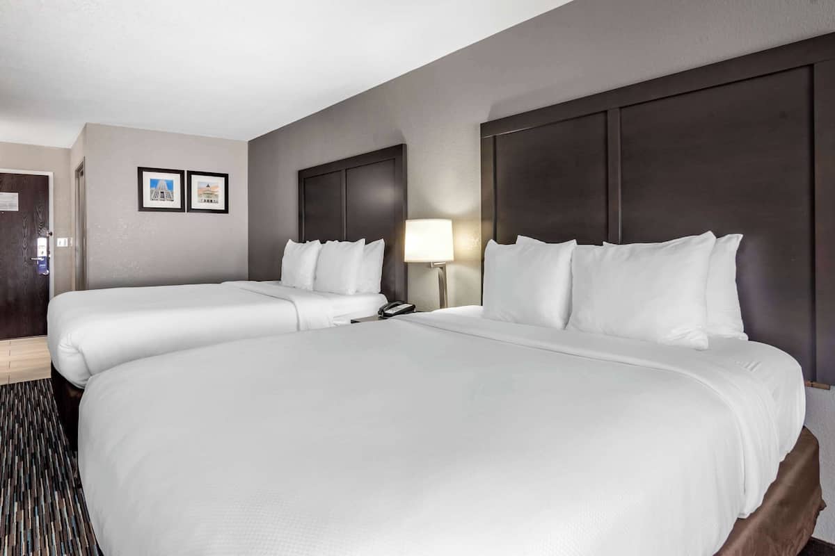 A hotel room with two beds, a bedside table with a lamp, and a door.