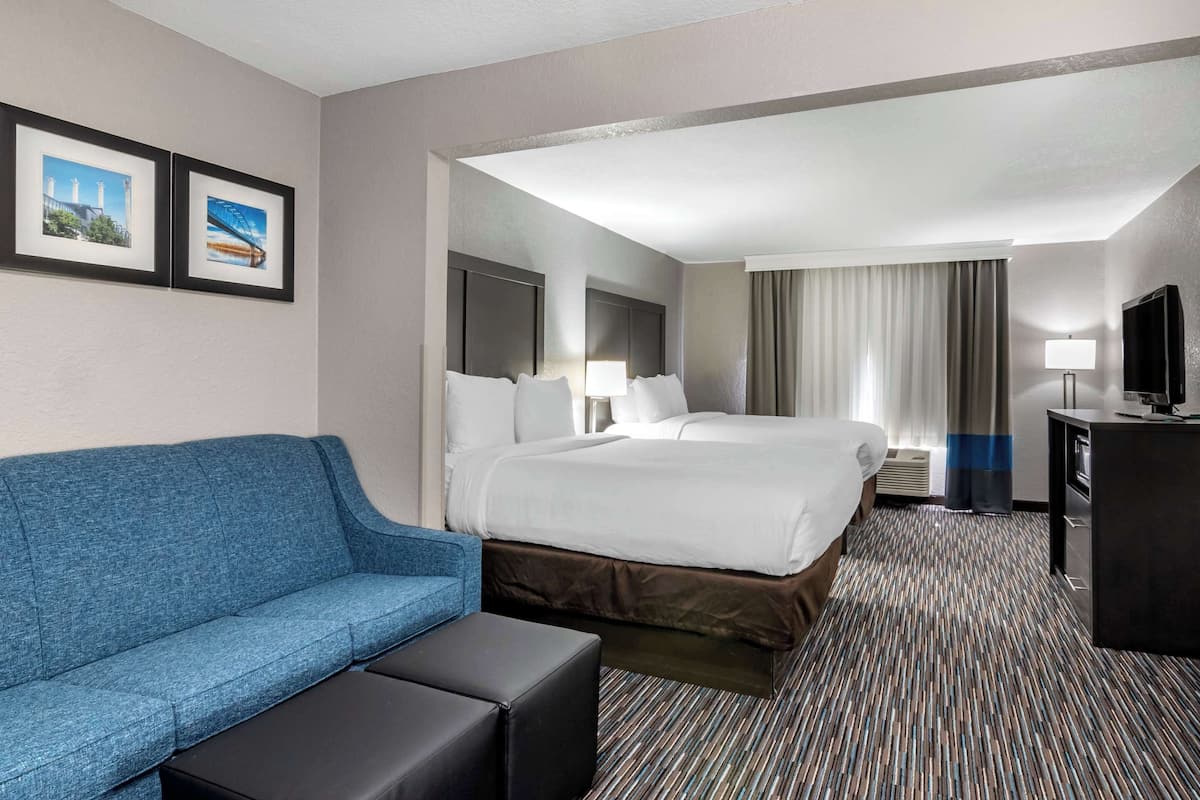 A hotel room with a large bed, a blue sofa, a small table, and a TV.