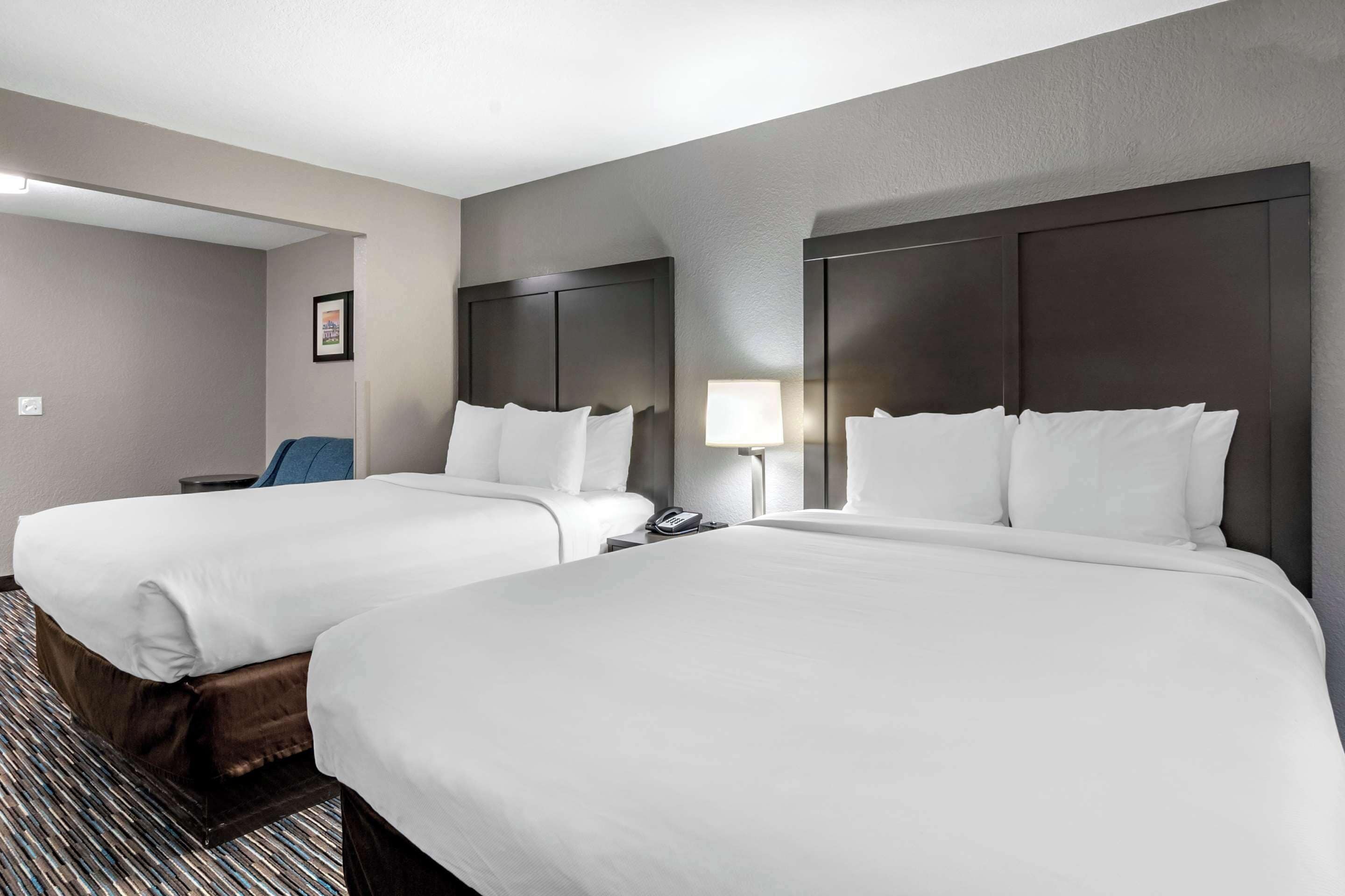 A hotel room with two beds, a desk, a chair, a lamp, and a framed picture on the wall.