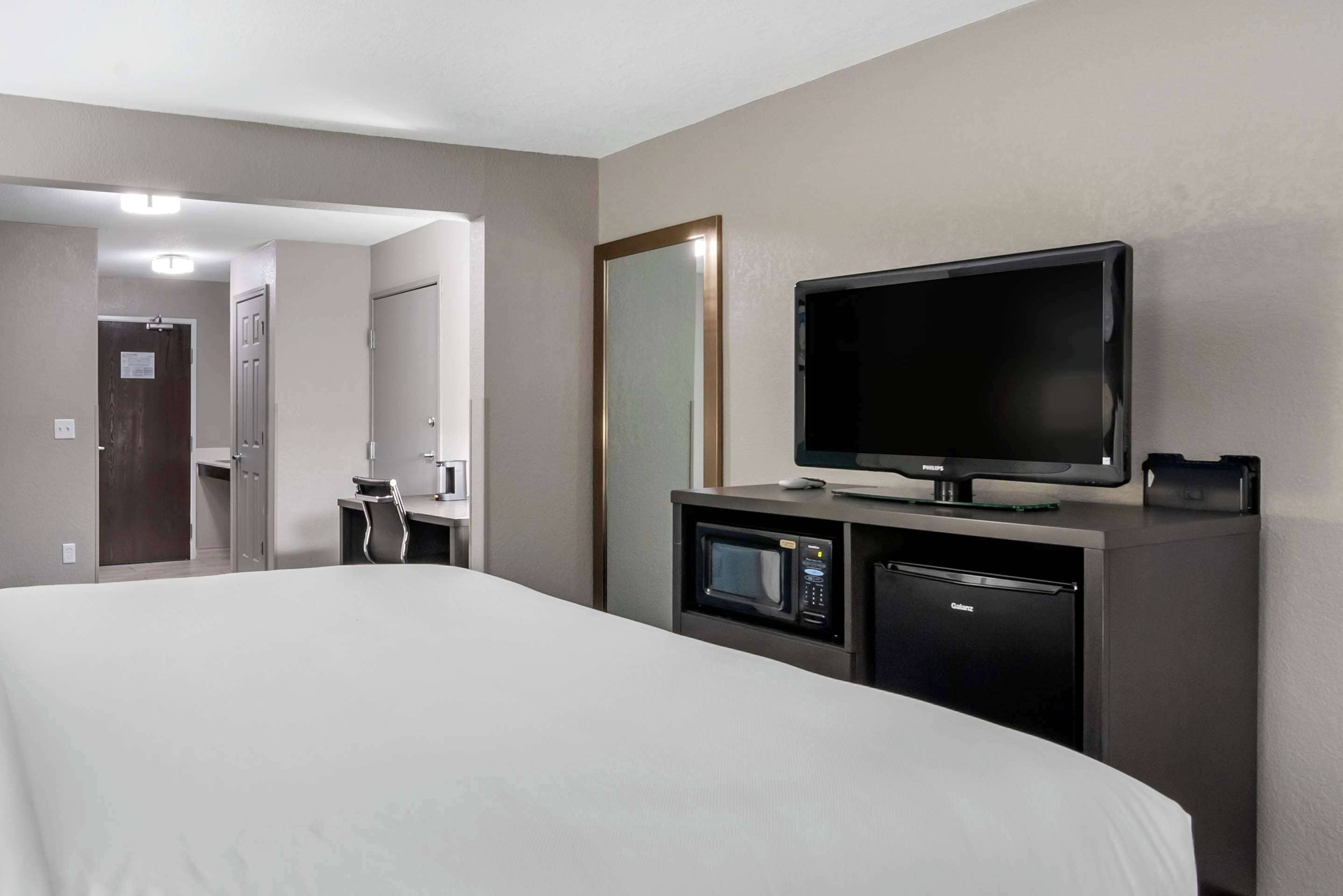 A hotel room with a large bed, a television, a microwave, and a refrigerator.