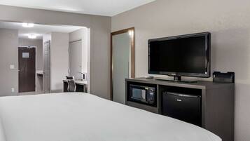 A hotel room with a large bed, a television, a microwave, and a refrigerator.
