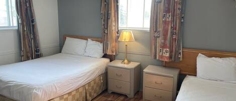 Une chambre d’hôtel avec deux lits, un plancher en bois et une fenêtre avec des rideaux.