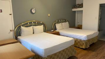 A room with two single beds, a wooden desk, a clock on the wall, and a small shelf above the bed.
