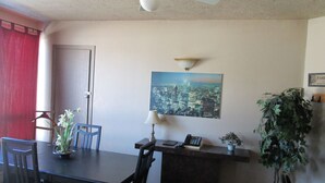 A dining area with a table, chairs, a ceiling fan, a wall-mounted lamp, a telephone, a small potted plant, and a framed cityscape picture. - Motel Lustre d'Or (Québec City)