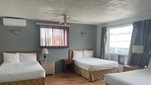 A hotel room with two beds, wooden flooring, a ceiling fan, a window with curtains, and a wall-mounted air conditioner. - Motel Lustre d'Or (Québec City)