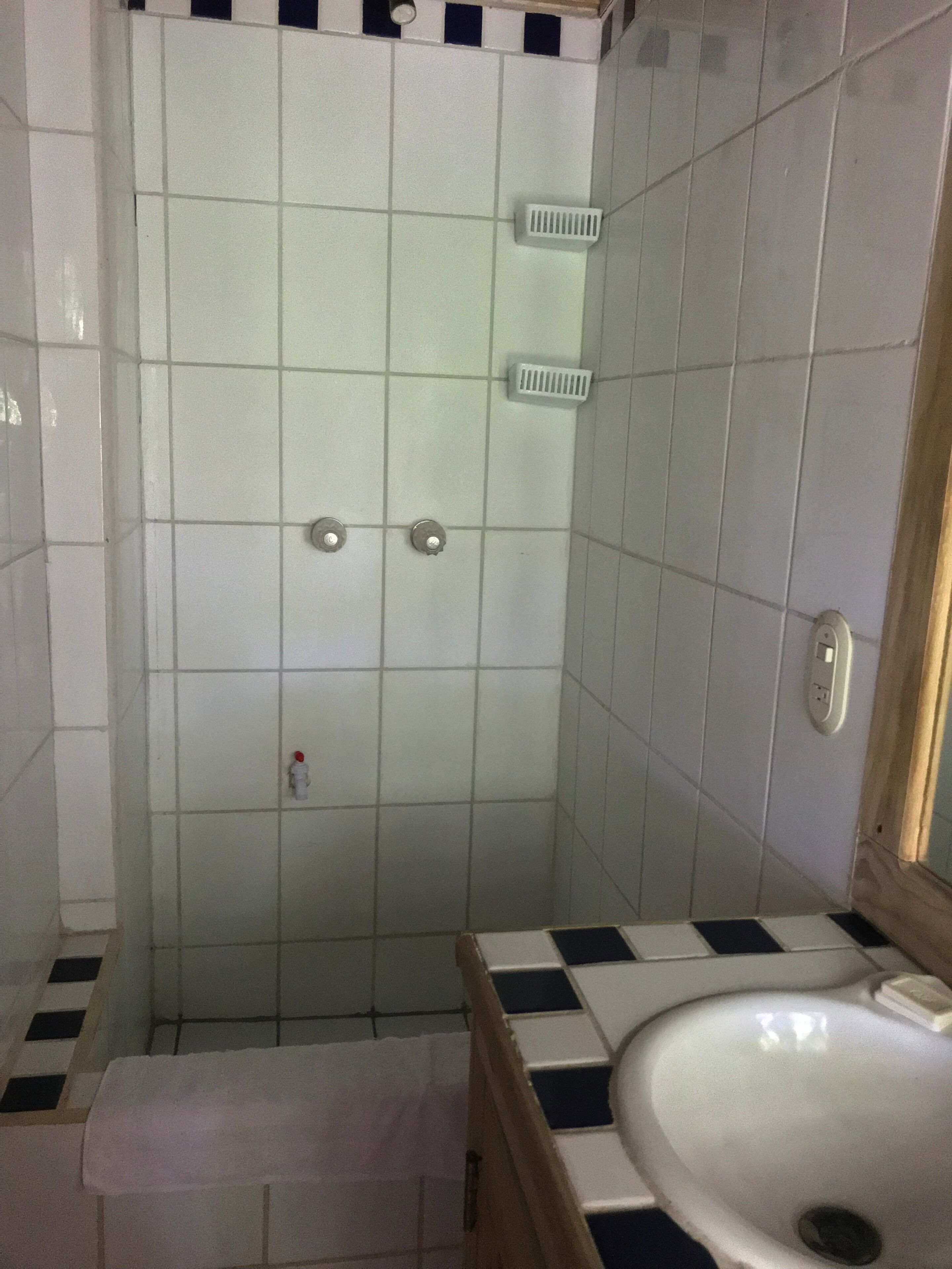 A bathroom with white tiled walls, a white sink with a black and white checkered countertop, and a shower area with a white vent.