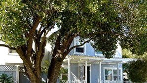 A house with a covered porch and a large tree in front. - Harbor Inn (Santa Cruz)