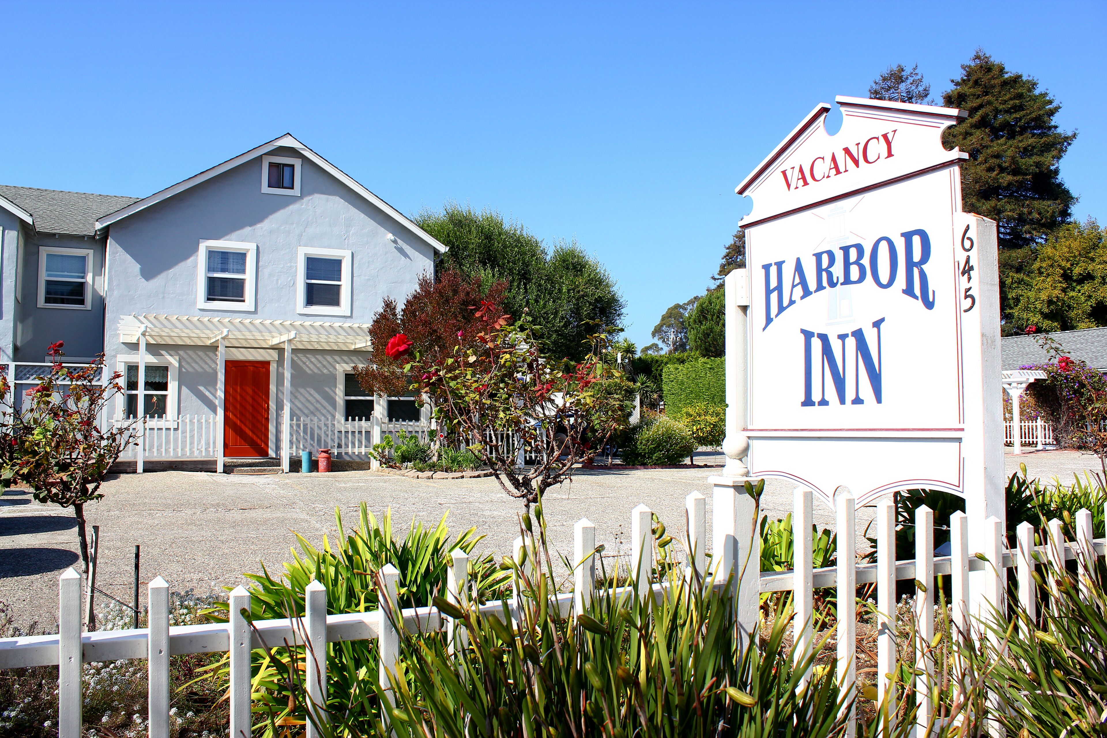 A two-story building with a red door and a white picket fence in front. A signboard with "Harbor Inn" and "Vacancy" is visible.