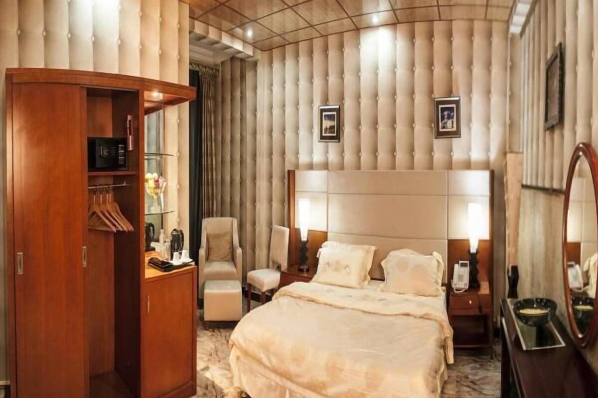 A hotel room with a large bed, a wooden wardrobe, a seating area with chairs, and a mirror on the wall.