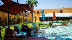 An outdoor patio with wicker furniture, a patterned floor, and umbrellas providing shade. - Royal Suites (Nouakchott)