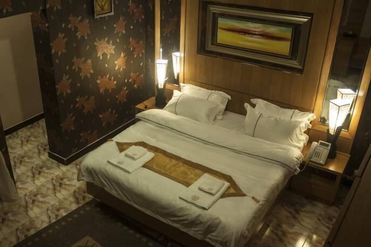 A hotel room with a large bed, two bedside tables, a nightstand, a wall-mounted TV, and a patterned carpet.