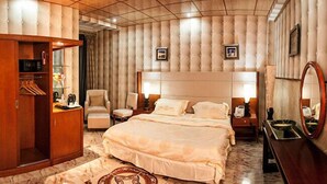 A spacious bedroom with a large bed, a wardrobe, a sitting area with chairs, and a vanity with a mirror. - Royal Suites (Nouakchott)