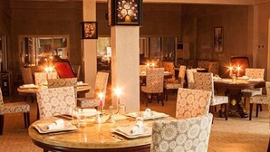A dining area with round tables and patterned chairs, candle-lit ambiance, and a central decorative piece. - Royal Suites (Nouakchott)