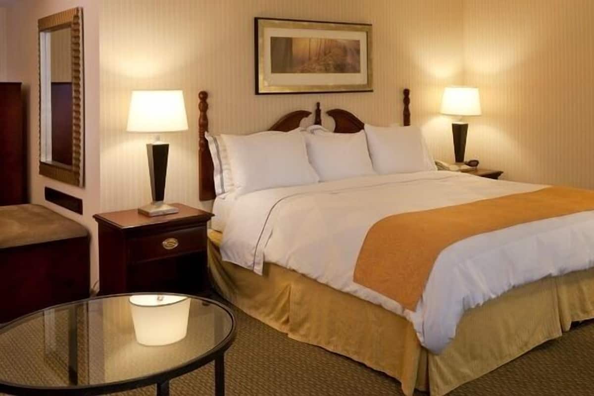 A hotel room with a large bed, two bedside tables with lamps, a round glass table, and a mirror on the left wall.