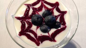 A glass bowl of dessert with blueberries and a red sauce, placed on a white surface.