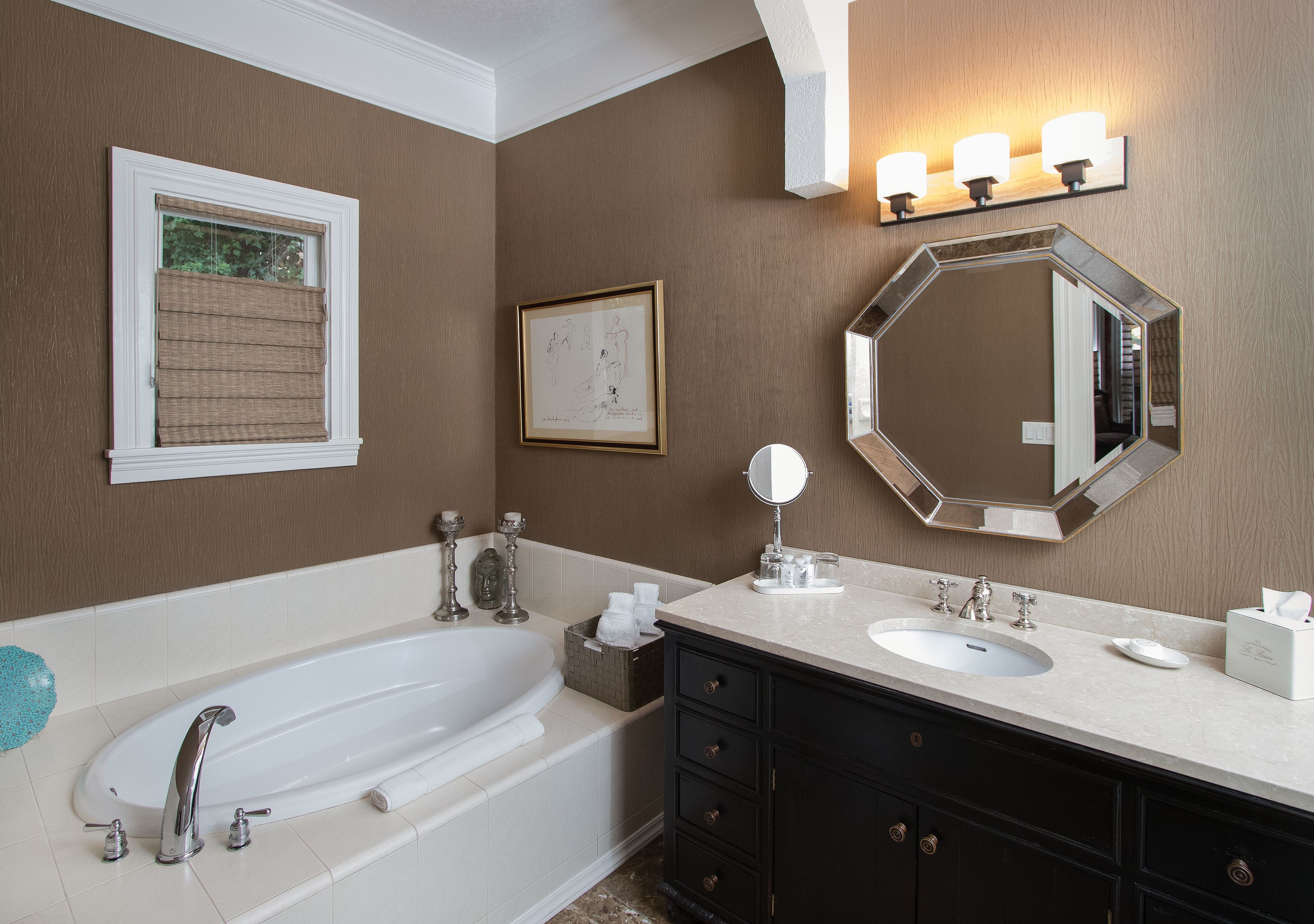 A bathroom with a bathtub, a sink, a vanity with drawers, a large mirror, and a wall-mounted light fixture.