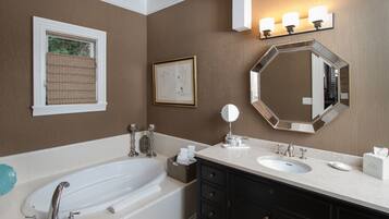 A bathroom with a bathtub, a sink, a vanity with drawers, a large mirror, and a wall-mounted light fixture.