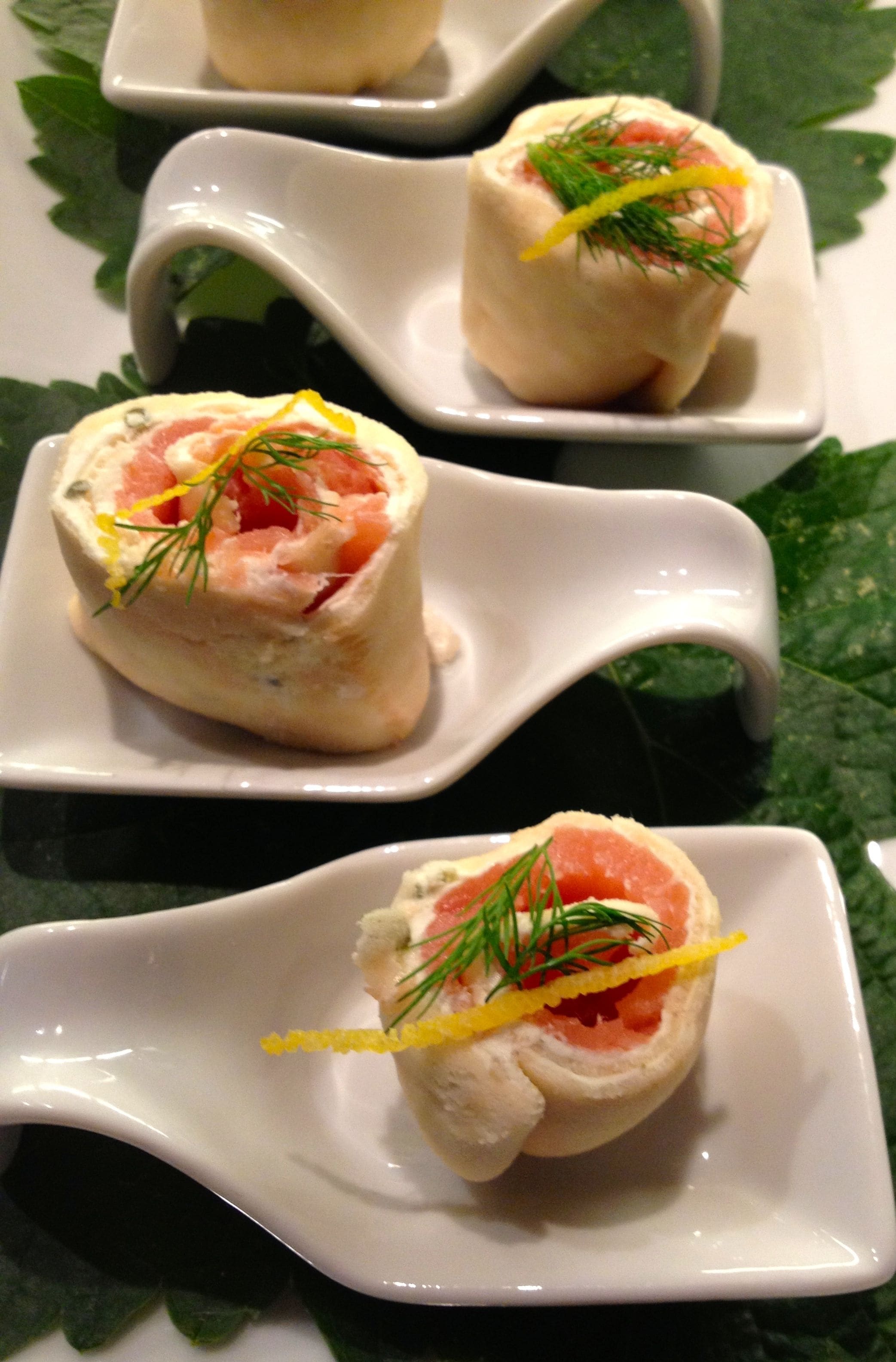 Three white square plates with a rolled appetizer featuring salmon and dill.