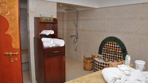 Un baño con un armario de madera, zona de ducha y una mesita con artículos de aseo.