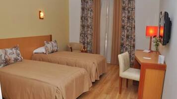 A hotel room with two beds, a desk, a chair, a TV, and curtains.