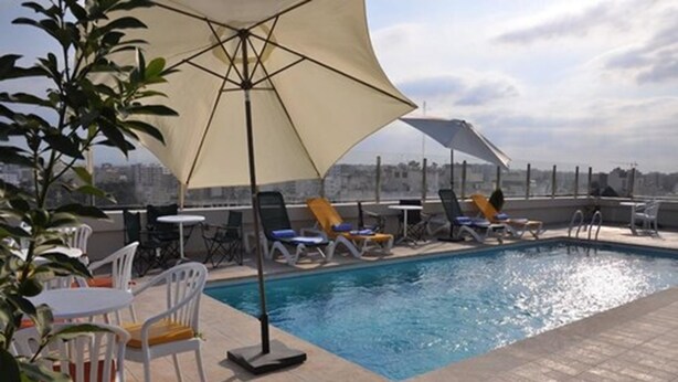 Un área de piscina en la azotea con sillones y sombrillas, rodeada de vistas urbanas.
