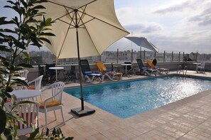 Un área de piscina en la azotea con sillones y sombrillas, rodeada de vistas urbanas.