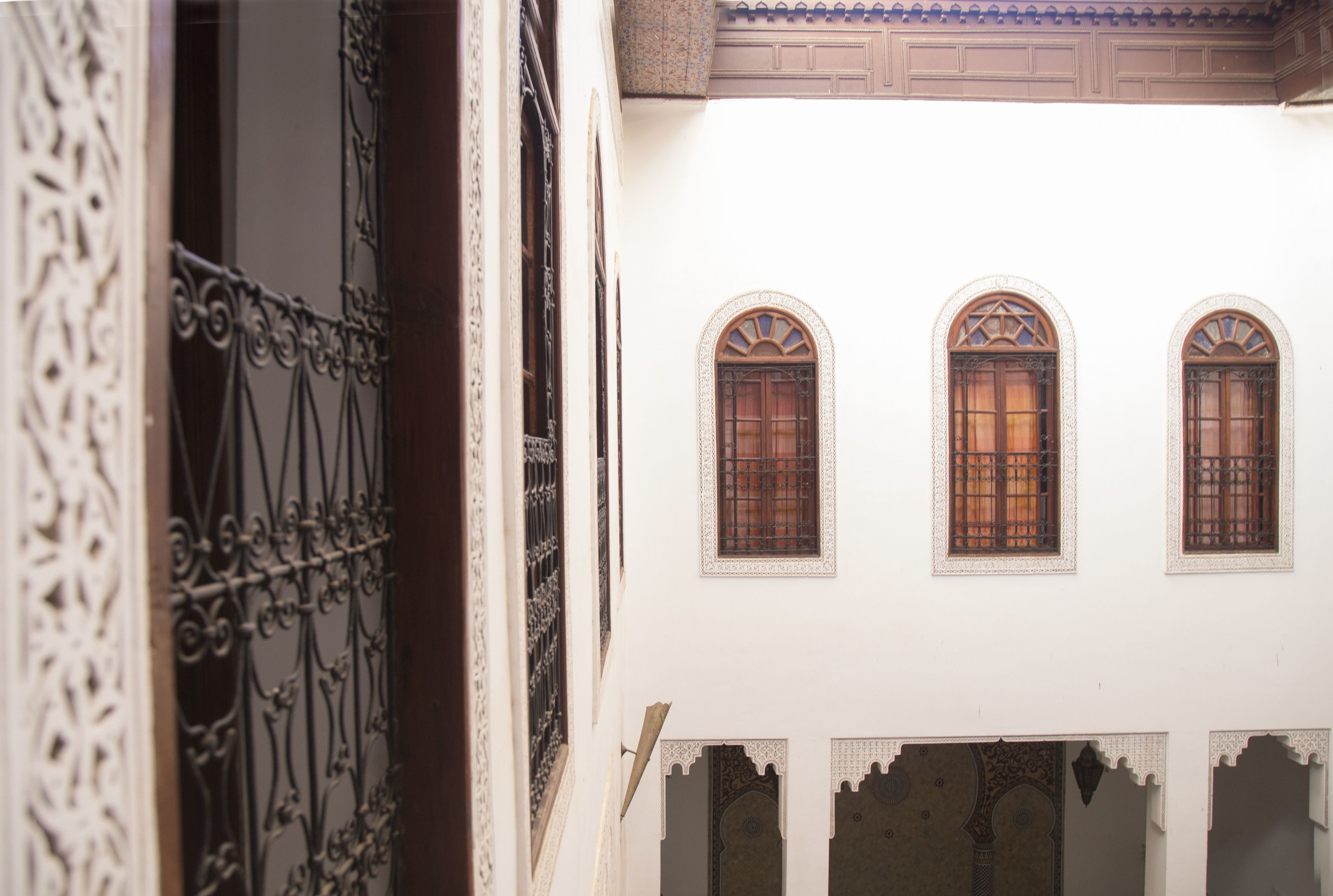 A courtyard with ornate iron gates and three arched windows with wooden shutters.