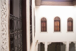 Um pátio com portões de ferro decorados e três janelas arqueadas com persianas de madeira.