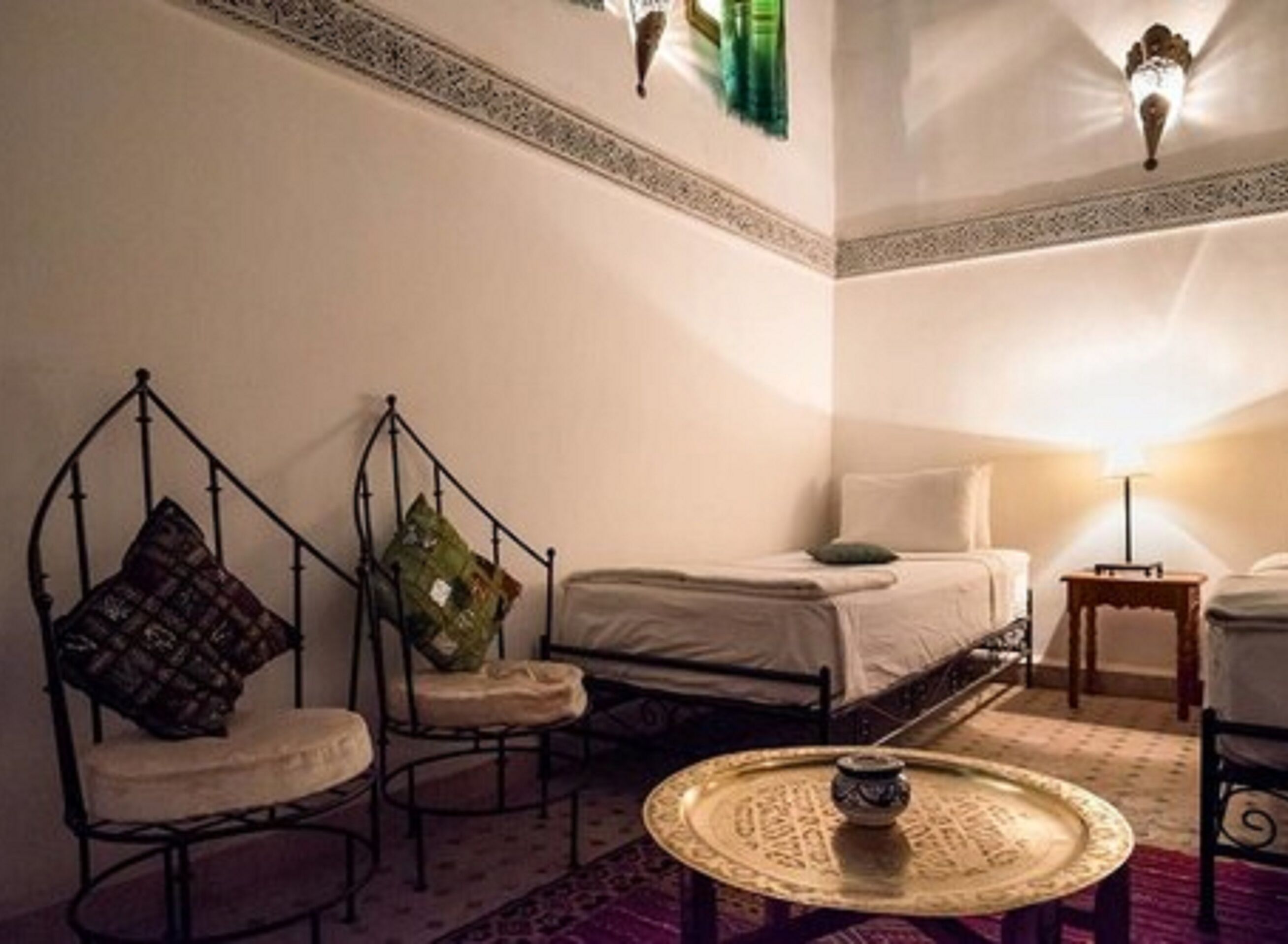A room with a bed, two chairs, a small table, and decorative wall sconces.