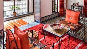 A Moroccan-style room with a red carpet, patterned cushions, and a table with a bowl. - Riad Jamaï (Fes)