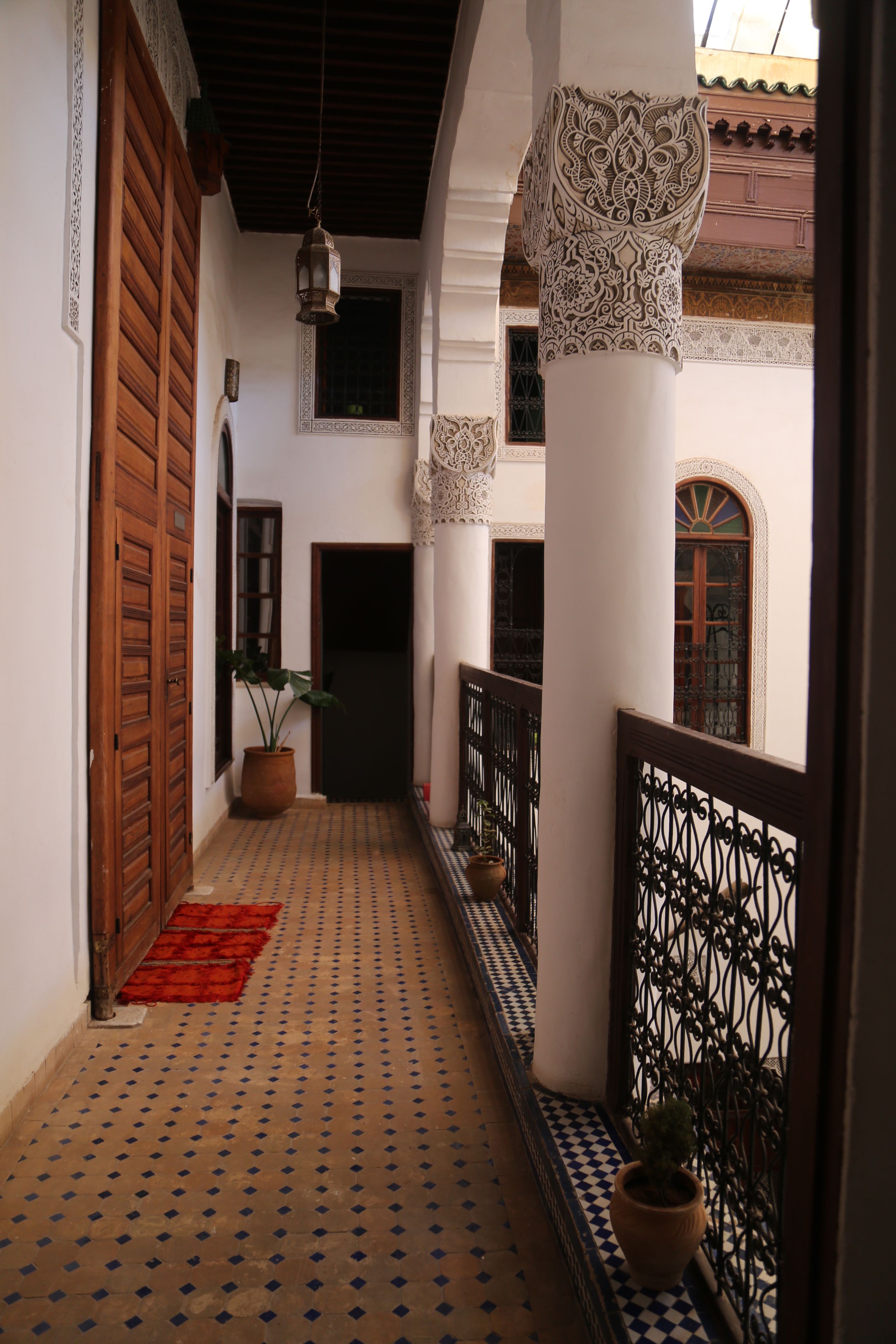 A corridor with patterned floor tiles, wooden doors, and a potted plant.