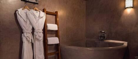 A bathroom with a large bathtub, wooden towel rack with robes, and a wall-mounted light fixture.