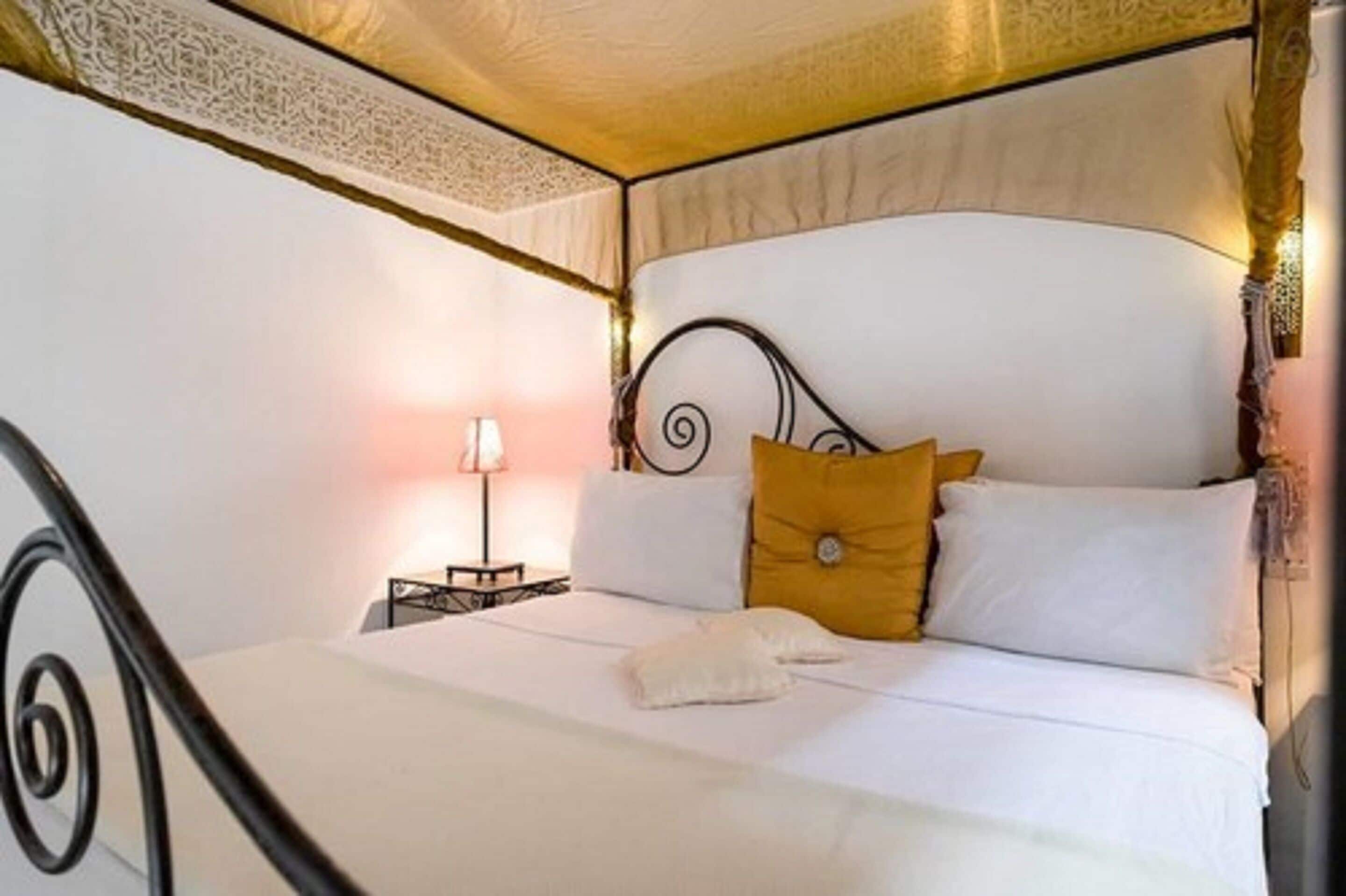 A neatly made bed with white linens and a single yellow pillow, a bedside table with a lamp, and a decorative headboard.