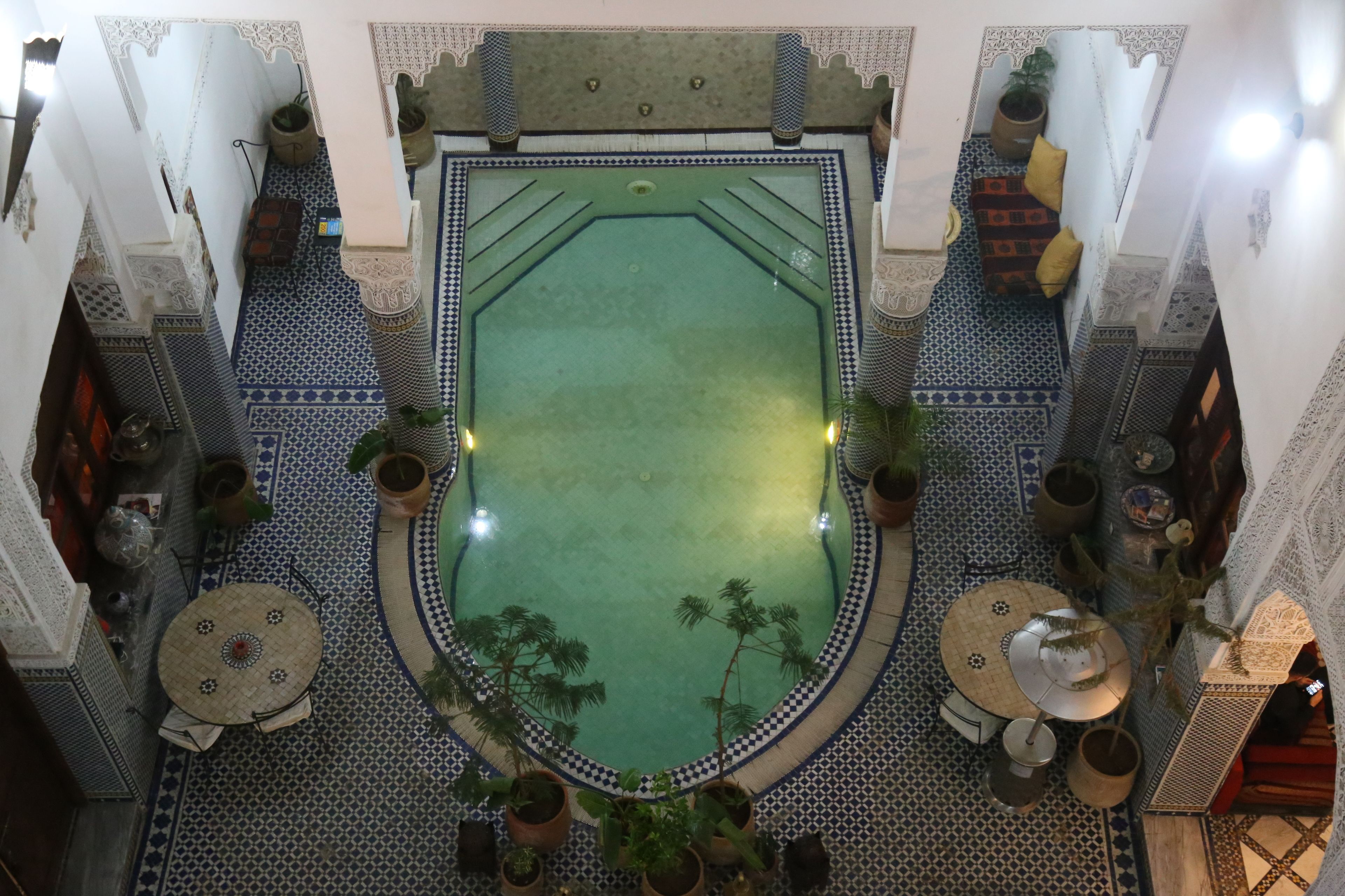 A courtyard with a central pool, surrounded by patterned tiles and potted plants.