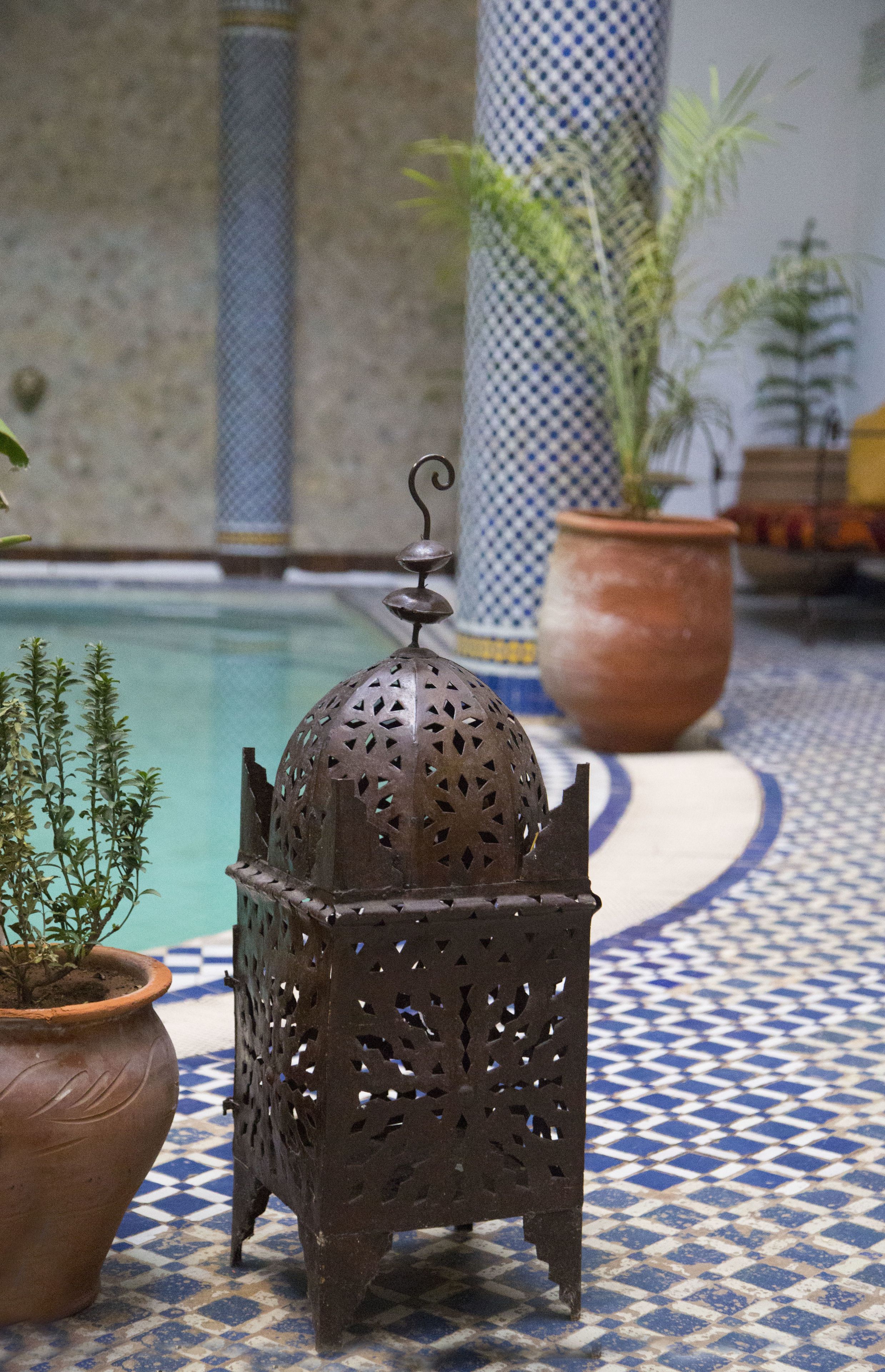 Een decoratieve metalen lantaarn met ingewikkelde uitgesneden patronen, geplaatst op een betegelde vloer met een blauw-wit ruitmotief.