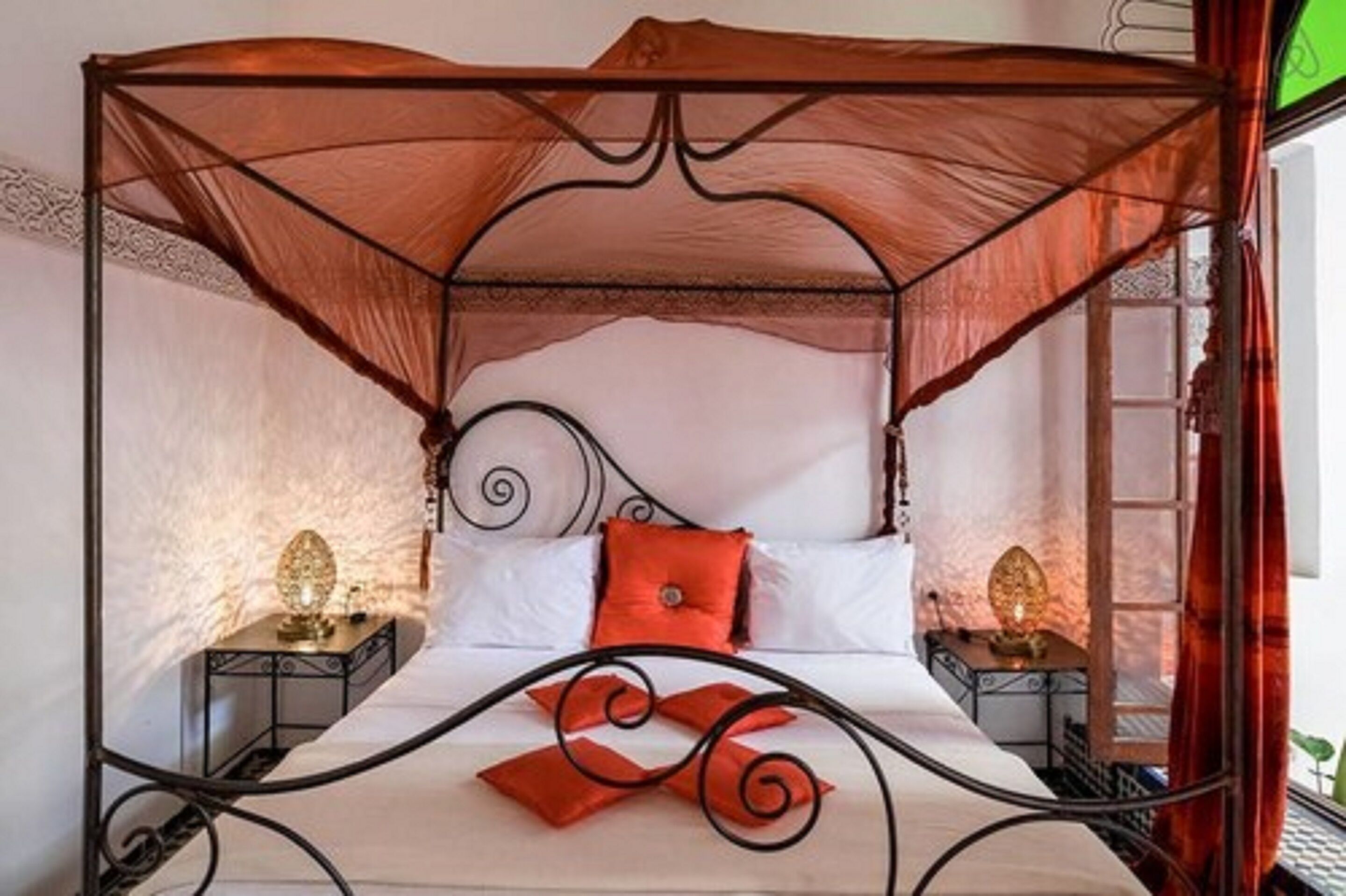 Uma cama de dossel com cortina, roupa de cama branca e duas mesas de cabeceira com abajures.